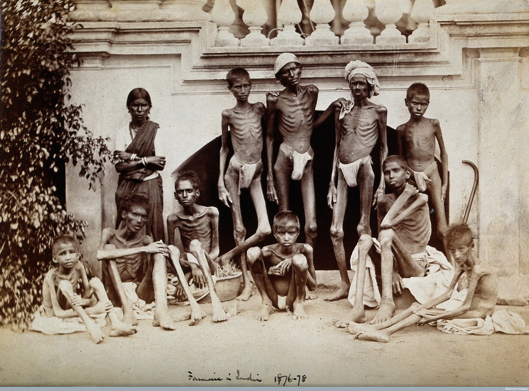 Historical photograph from the Indian famine of 1876–78 showing a group of severely emaciated men and children, photographed by Willoughby Wallace Hooper.
